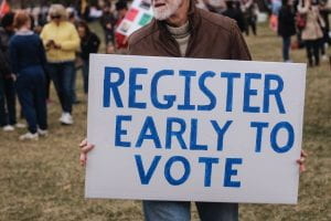 Man holding a sign that says, "Register Early to Vote."