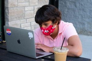 Adria, wearing a mask and working outside on her laptop.