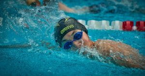 Thephotoshows a young woman wearing goggles and a swim cap doing laps in a swimming pool.