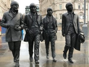 Life-sized bronze statues of The Beatles walking down a sidewalk.