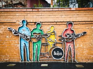 Photo shows metal art on a brick wall displaying the four Beatles with their instruments.