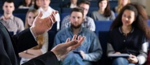 a professor lecturing to a group of college students sitting in class 