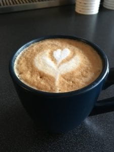 View of top of coffee mug with a plant and heart drawn into the latte foam. 