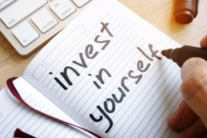 Man is writing "invest in yourself" in a notebook.