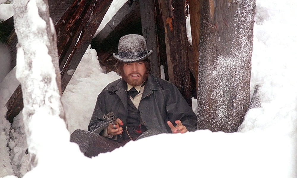 Warren Beatty holds a gun and sits in the snow