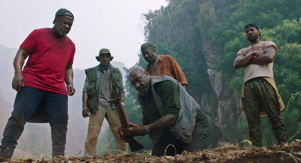 A group of men look at the ground in a jungle