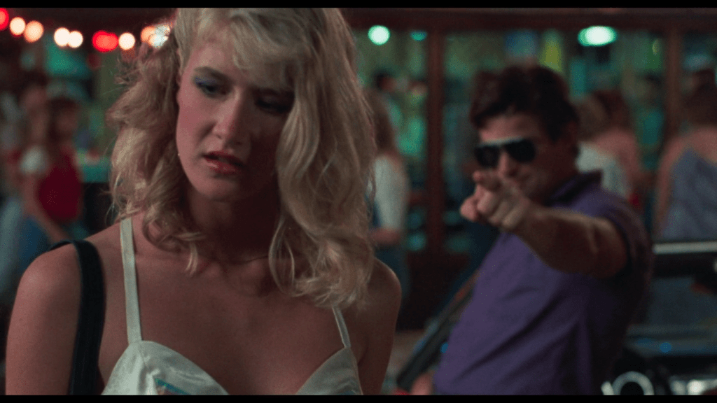 a man in sunglasses points menacingly at Connie, a blonde teenager played by Laura Dern