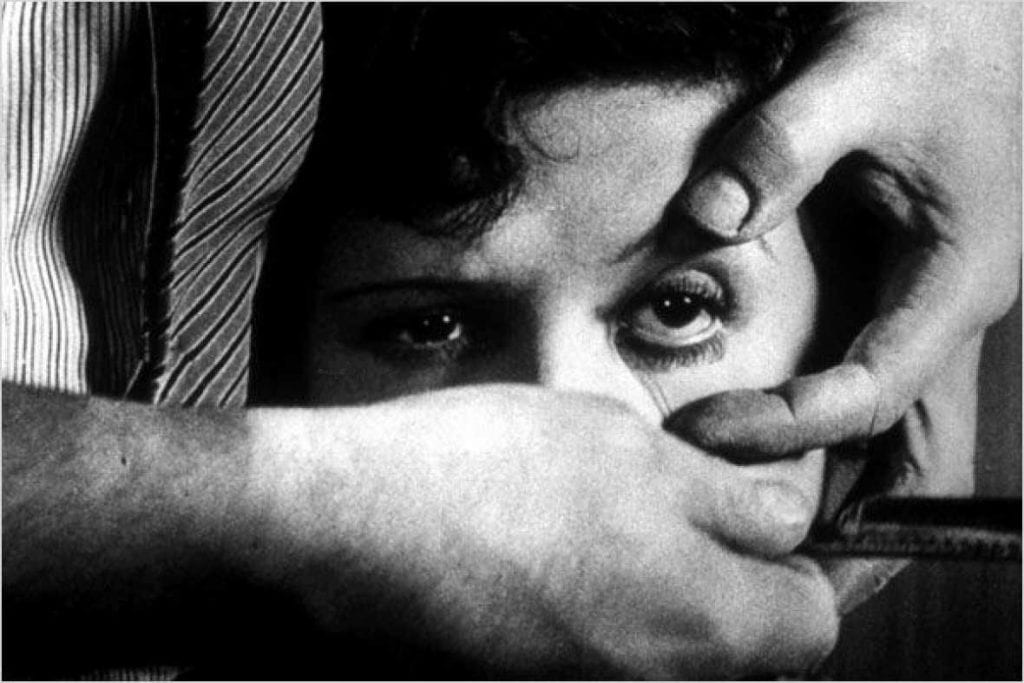 a man holds a woman's eye open with his fingers and holds a razor under her eye