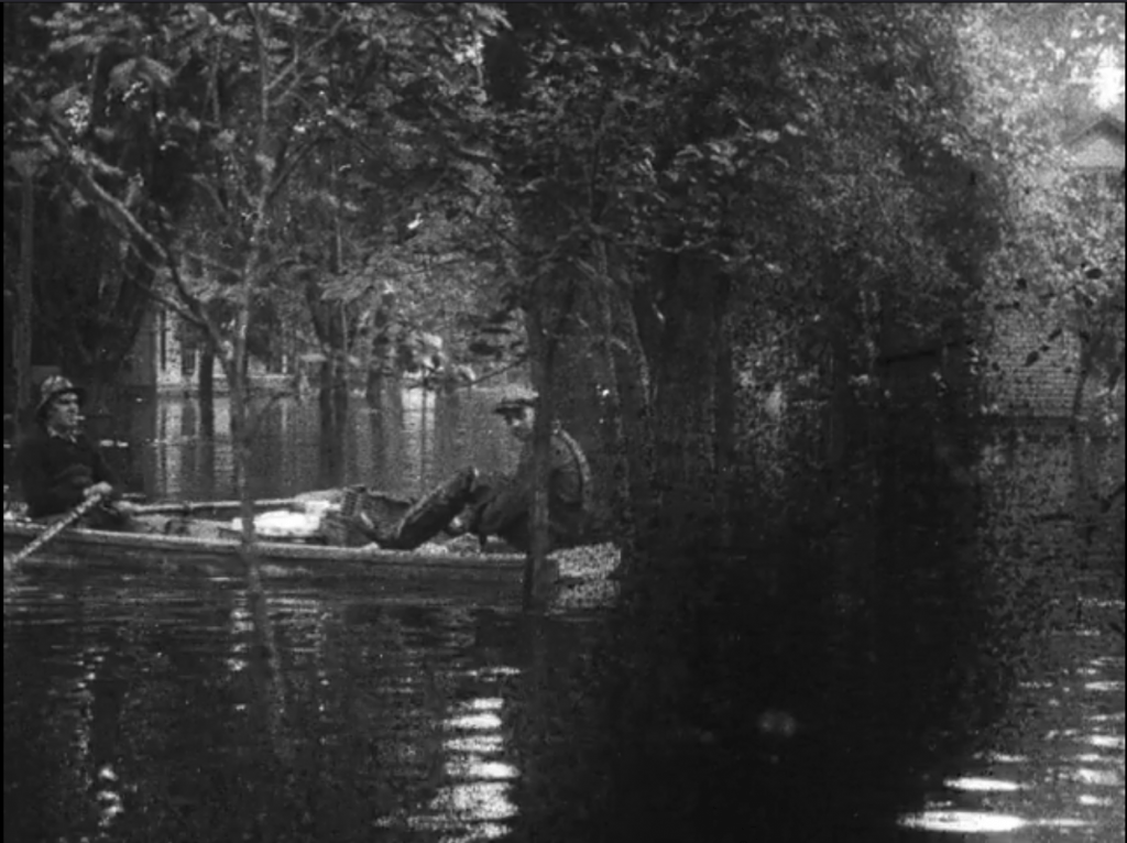 men row a boat through flooded streets. film deterioration on the right of the screen