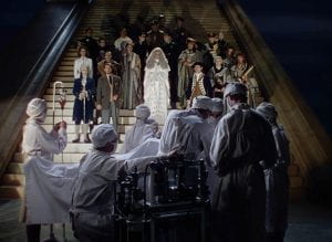 Historical figures gathered on stairs as they watch a surgery take place