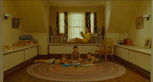 Three little boys listen to a record player on the floor while their sister sits and reads behind them