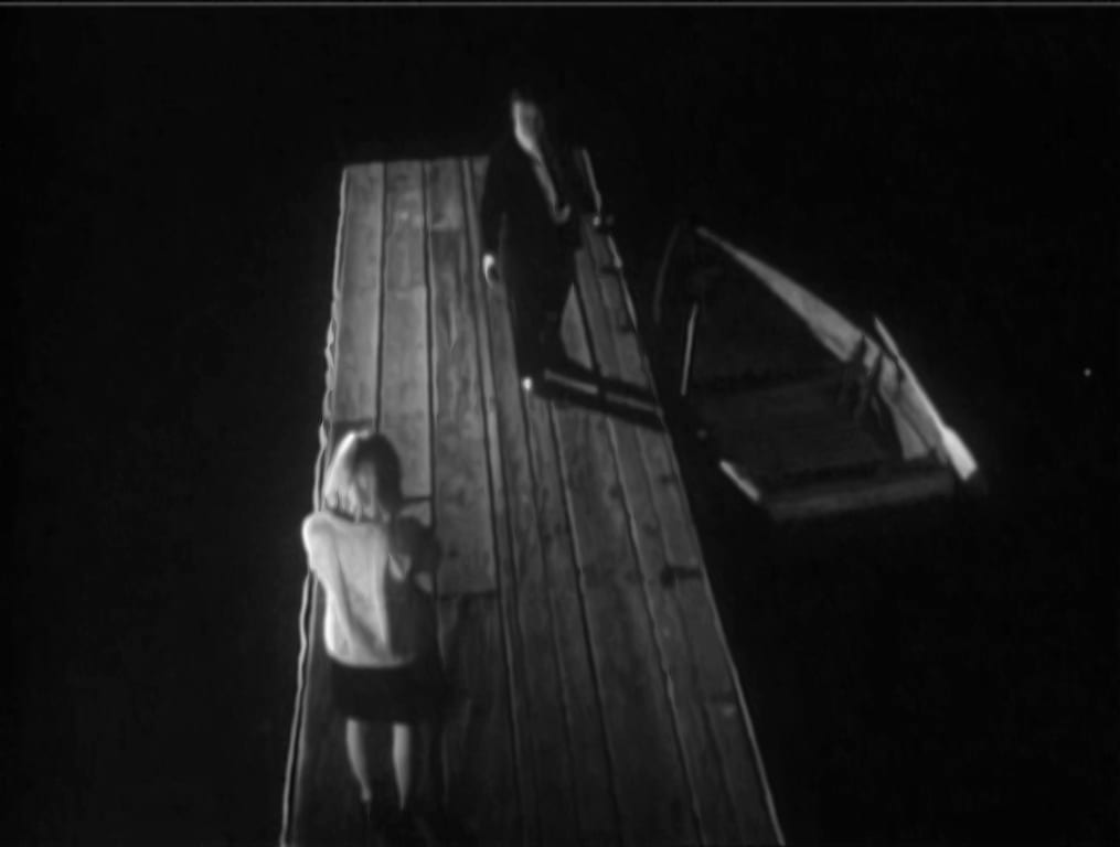 A man walks toward a woman on a boat dock at night