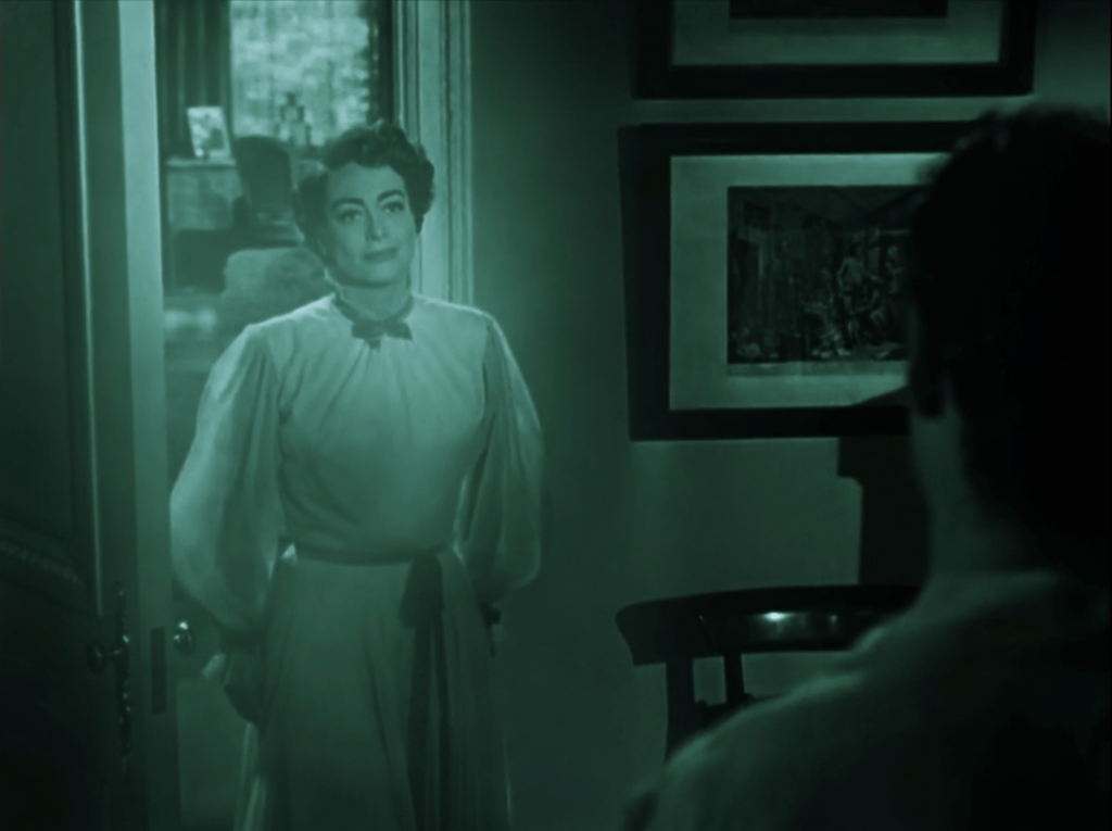 A woman stands in a doorway, bathed in green light