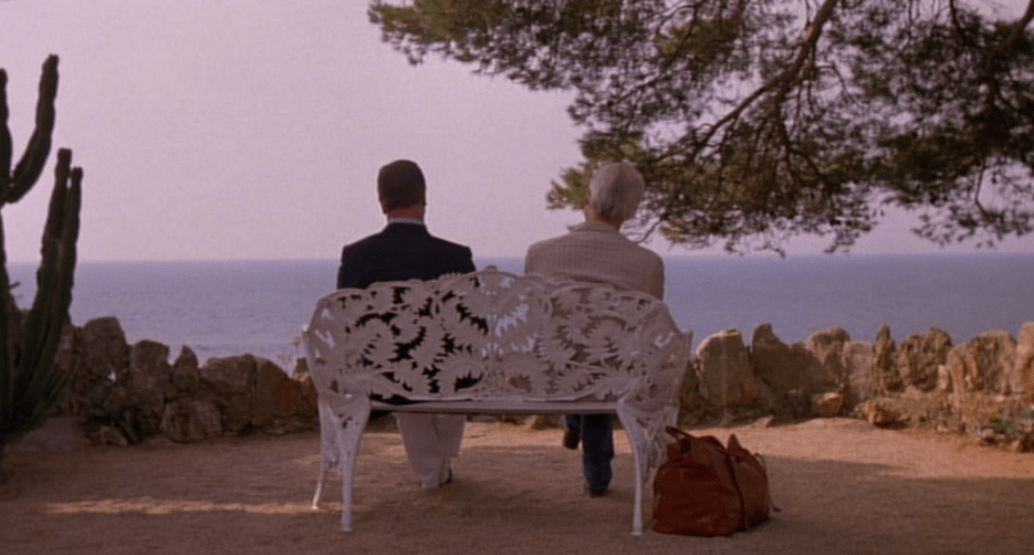 Two men sit on a bench in front of the ocean