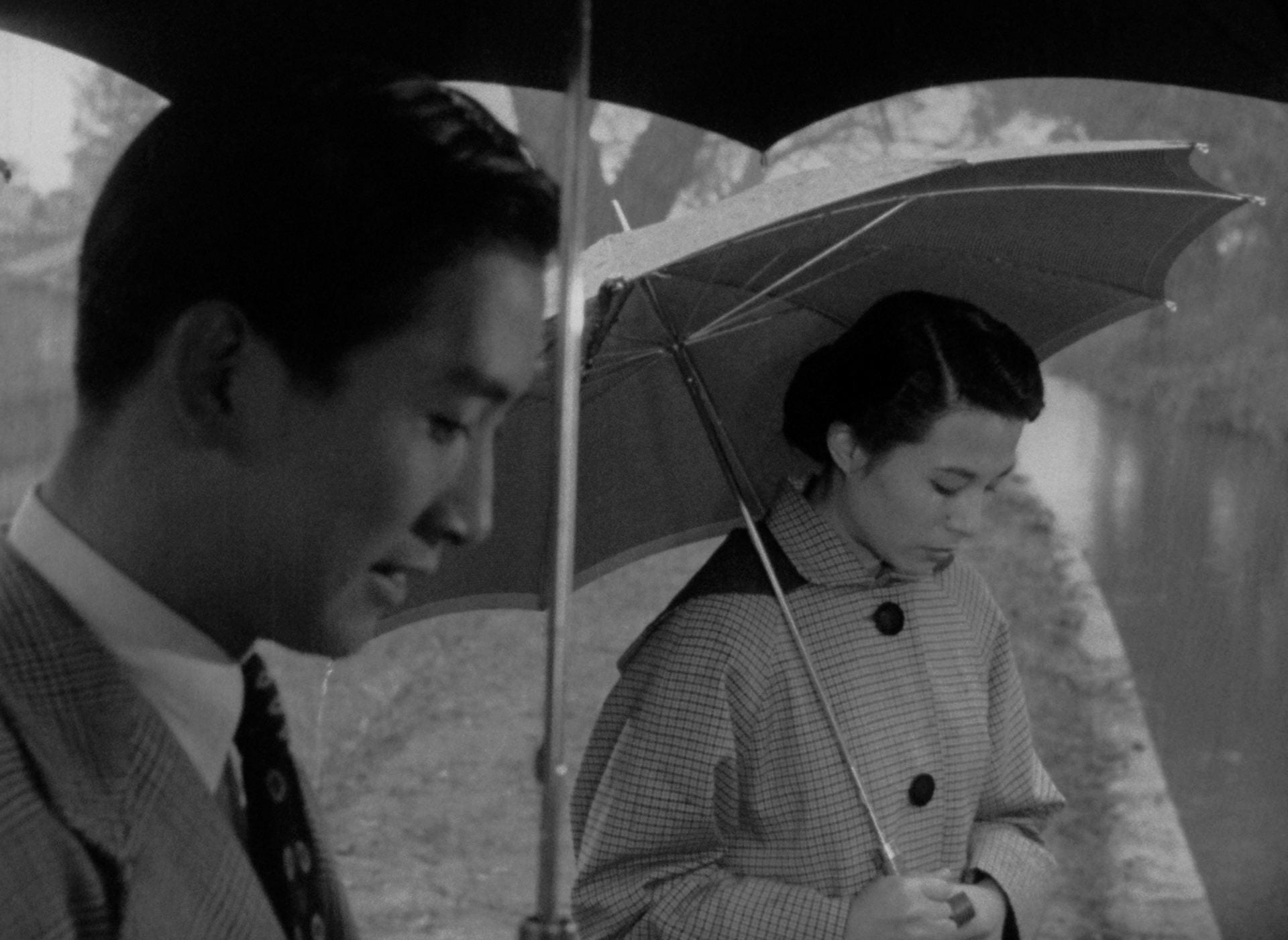 A man and woman stare at the ground, holding umbrellas