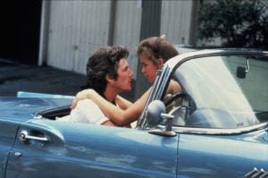 A woman sits on a man's lap in a blue classic car