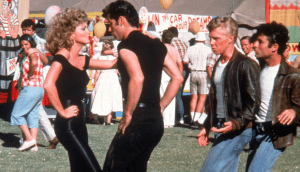 A man and woman in tight black clothes dance together in the midst of a crowd