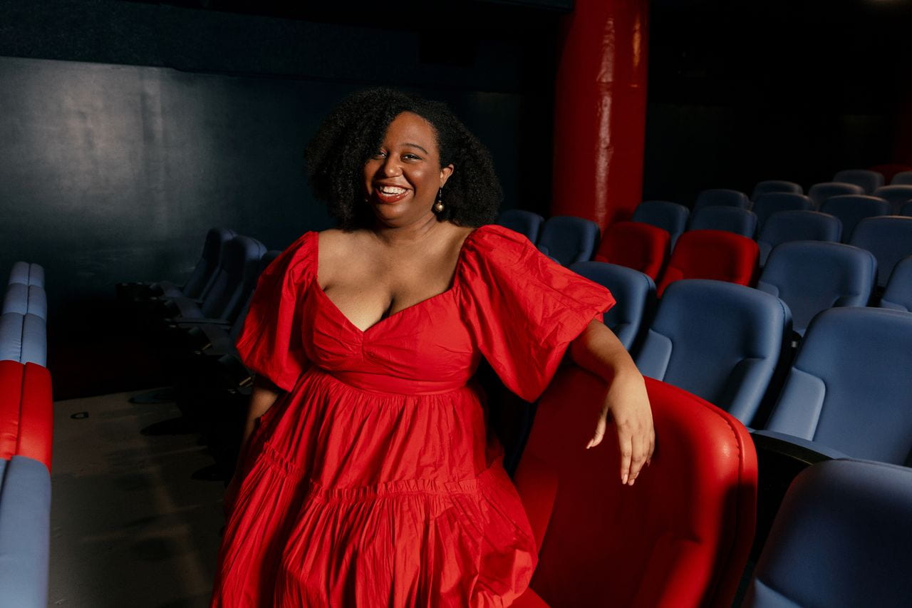 A woman in a bright red dress inside a movie theater with red and blue seats
