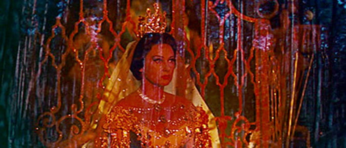 A woman with an elaborate headpiece and costume is shrouded in orange light