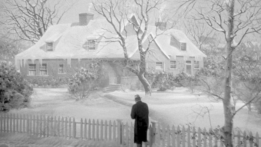 A man walks toward a house covered in snow