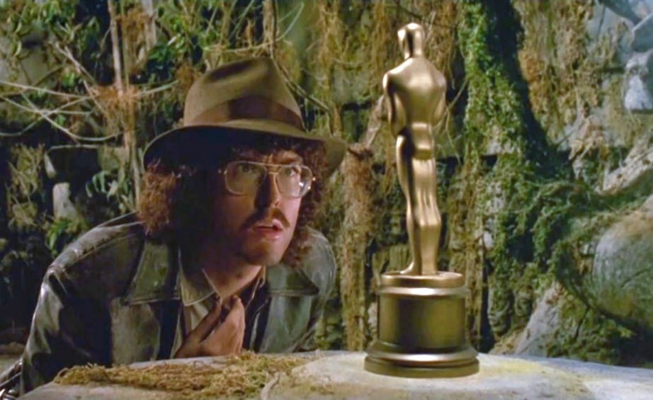 A bespectacled man in a cave looks at an Academy Award statuette in a spoof of Indiana Jones