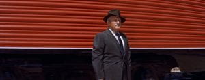 A man in a suit and hat stands in front of a red train car