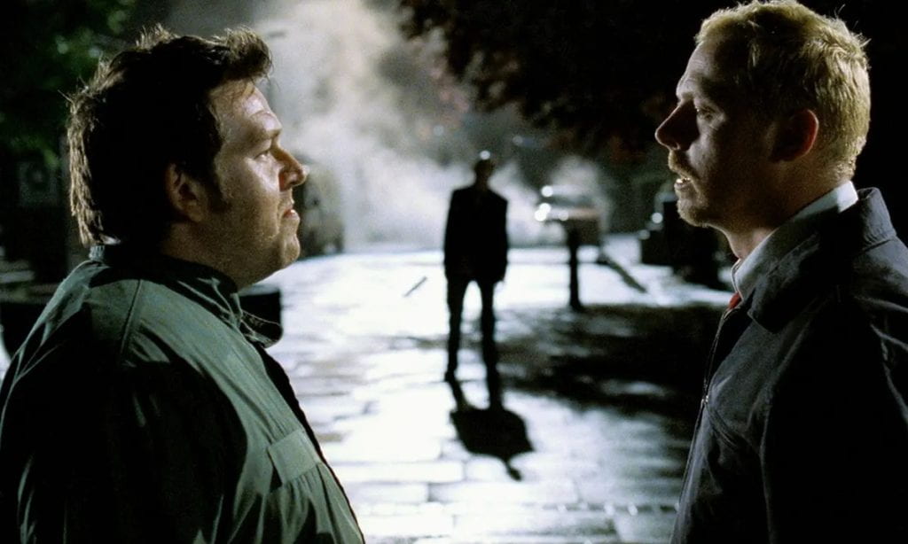 Ed and Shaun look at each other on a dark street while a figure stands between them in the distance
