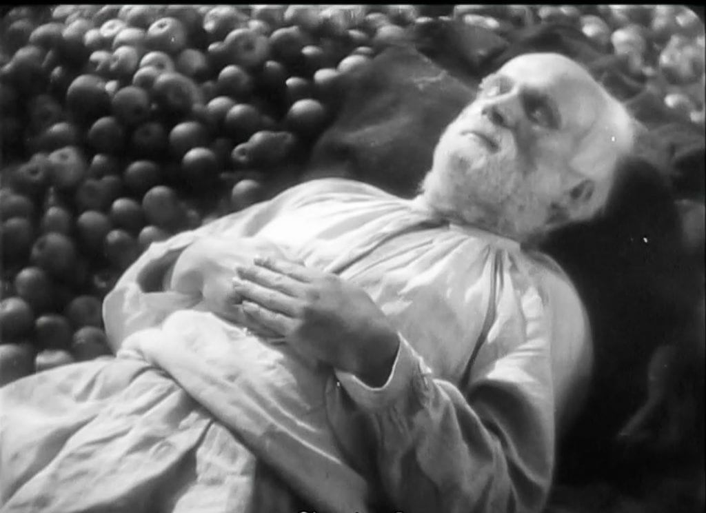 An old man rests on a pile of apples