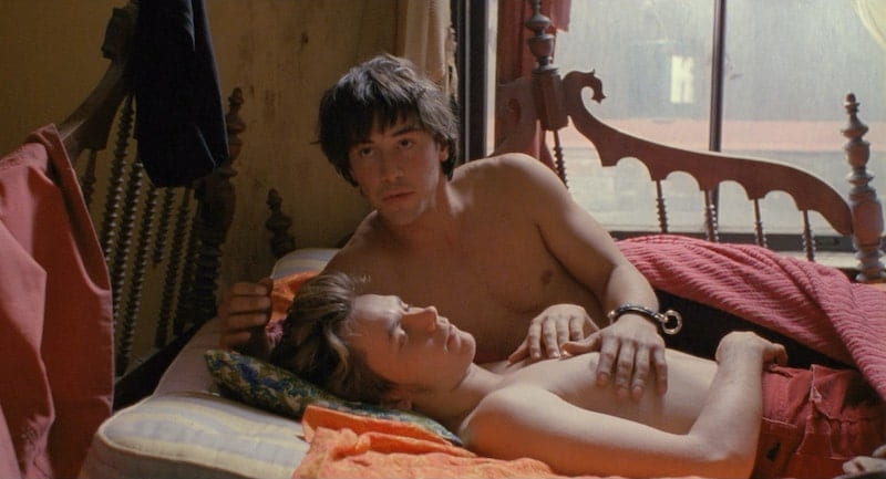 Keanu Reeves and River Phoenix lay in a bed together while shirtless