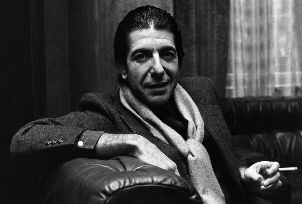 Black and white image of Leonard Cohen smoking and sitting on a couch