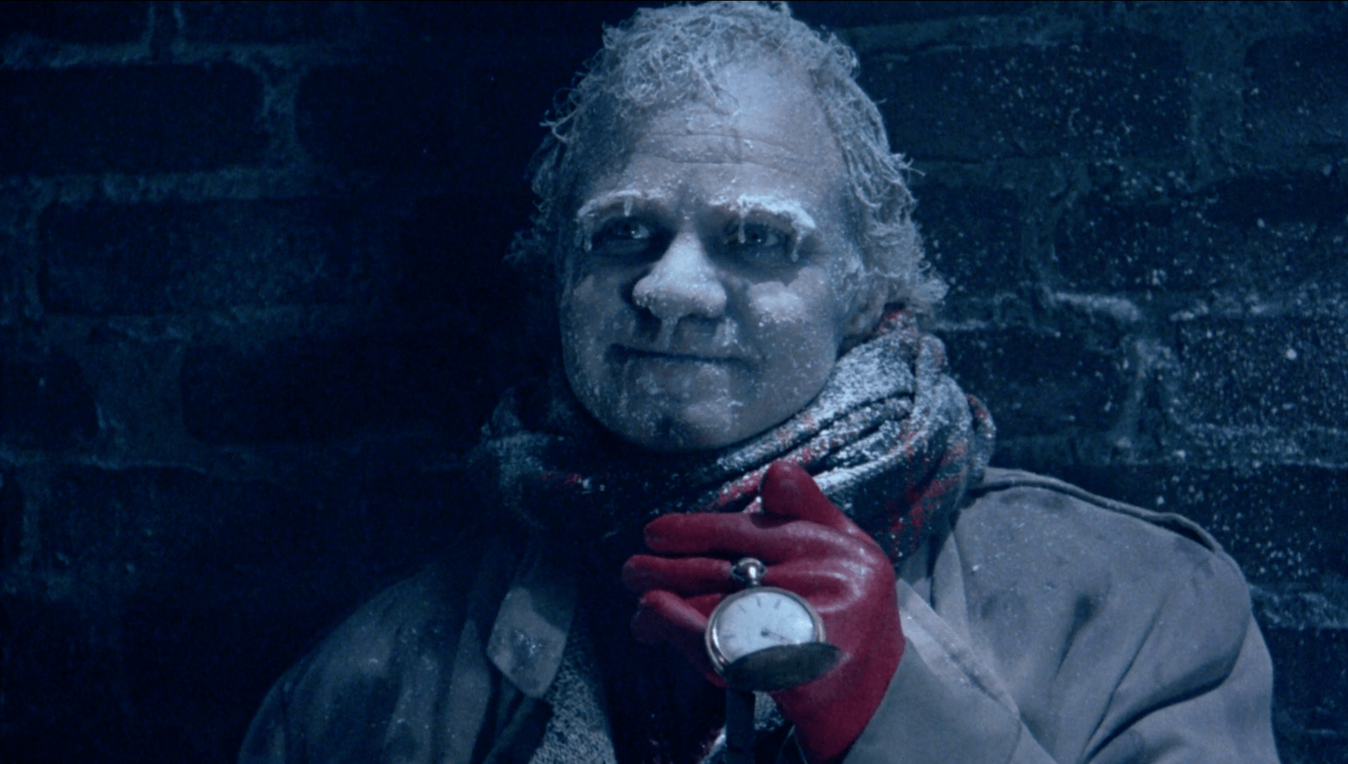Close-up of Herman, frozen and smiling. Ice is crystalized in his hair and eyebrows. His pocket watch hangs in mid-air from his hand, clothed in a red leather globe.