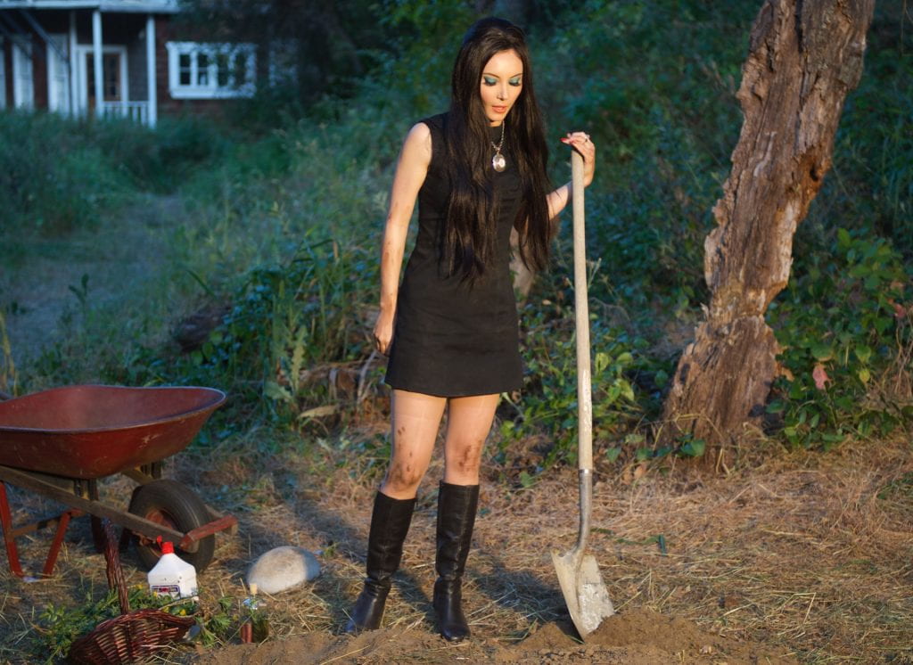 Elaine holding a shovel and looking down at a grave