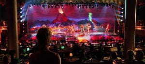 An audience watches a show onstage that includes fake volcanoes and dancers
