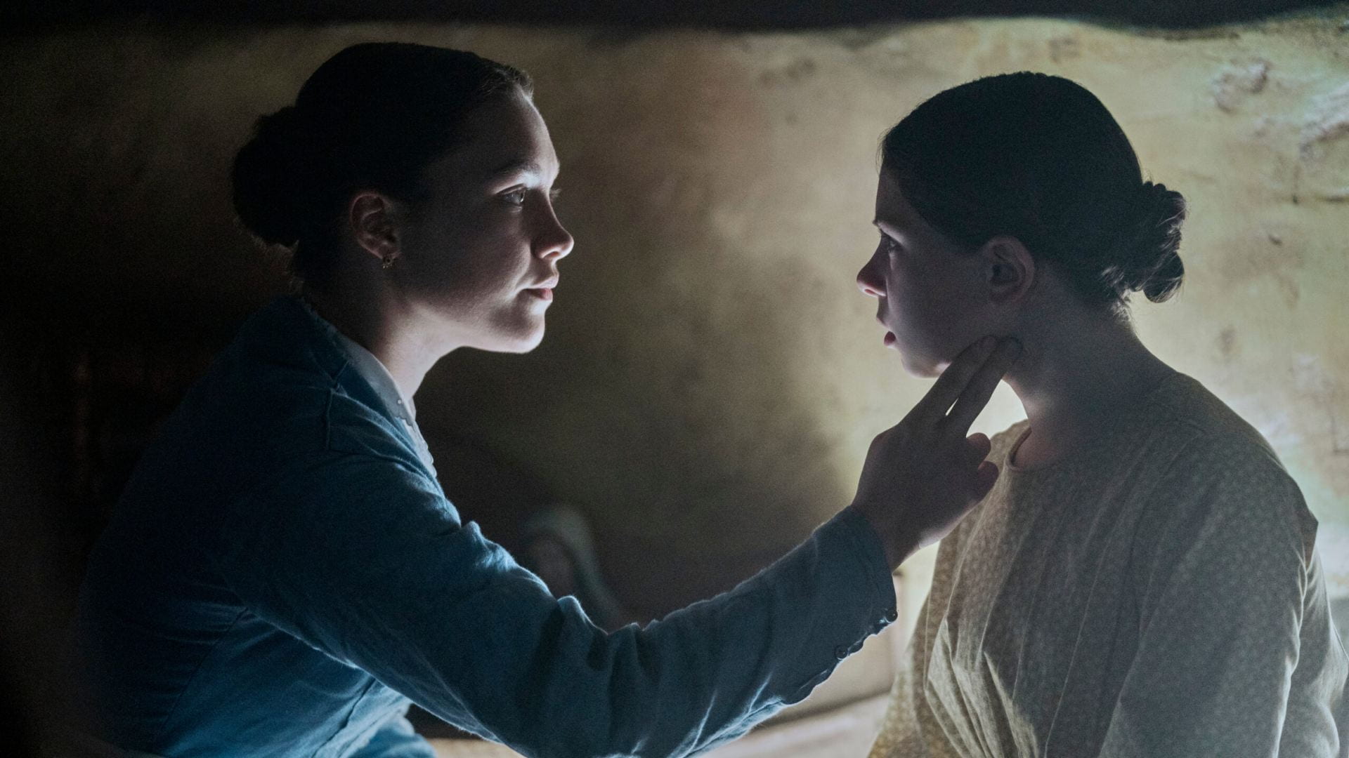 Florence Pugh and a young girl look at each other in a shadowy room