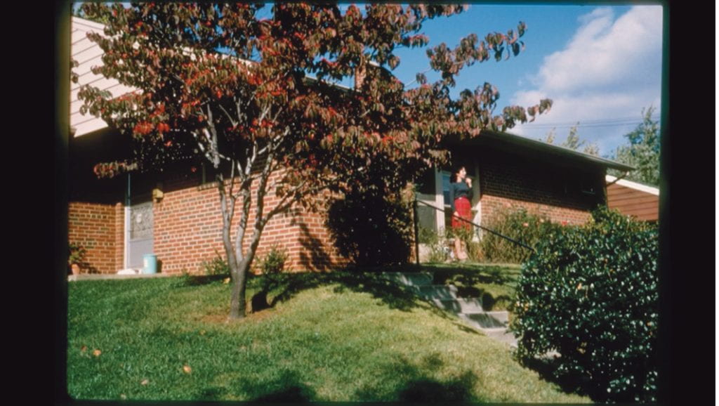 A woman stands in the distance in front of a brick house