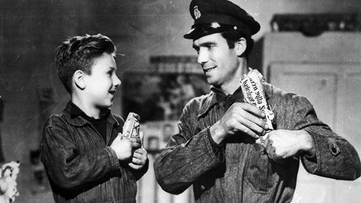 Screenshot from Bicycle Thieves. Ricci and his son Bruno smile at each other, putting sandwiches in their pockets while they get ready for work