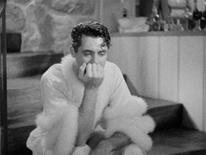 Cary Grant in a fuzzy women's robe as he sits exhausted on a staircase