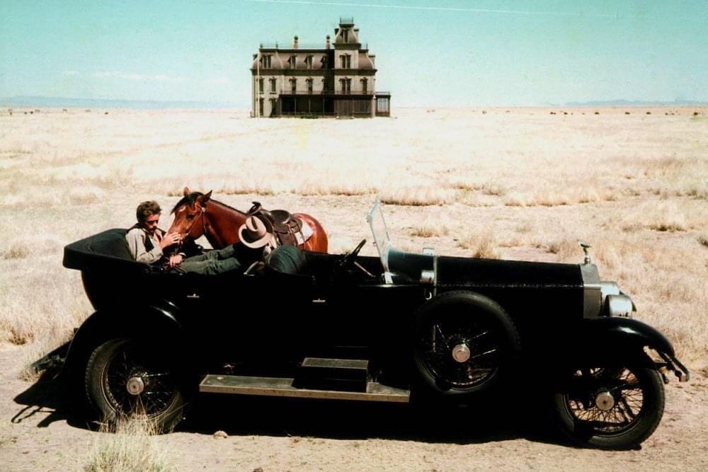 James Dean sits in a car while feeding a horse in an expansive Texas landscape