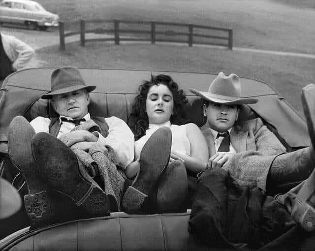Paul Mix, Elizabeth Taylor, and Rock Hudson sit together with their eyes closed and their feet up in the backseat of a car
