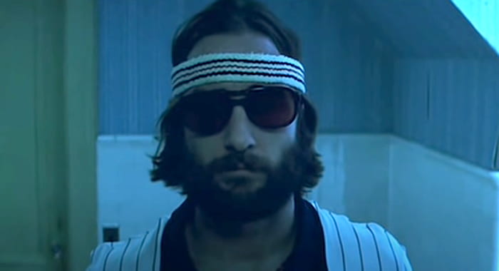 Close-up of Luke Wilson wearing sunglasses and a headband as he looks in a bathroom mirror