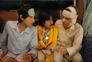 Adrien Brody, Jason Schwartzman, and Owen Wilson sit on a bed in a train car and look at each other in their pajamas