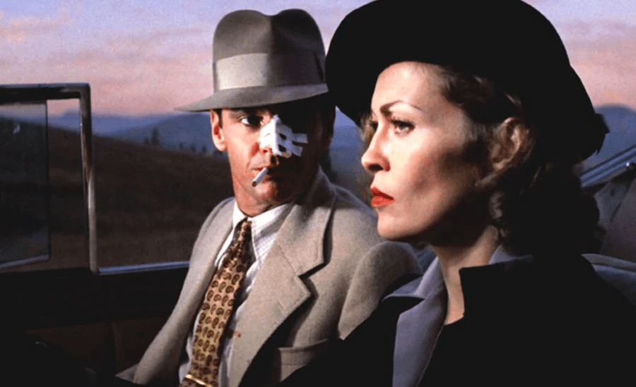 Jack Nicholson, with a bandaged nose, looks over at Faye Dunaway as she drives