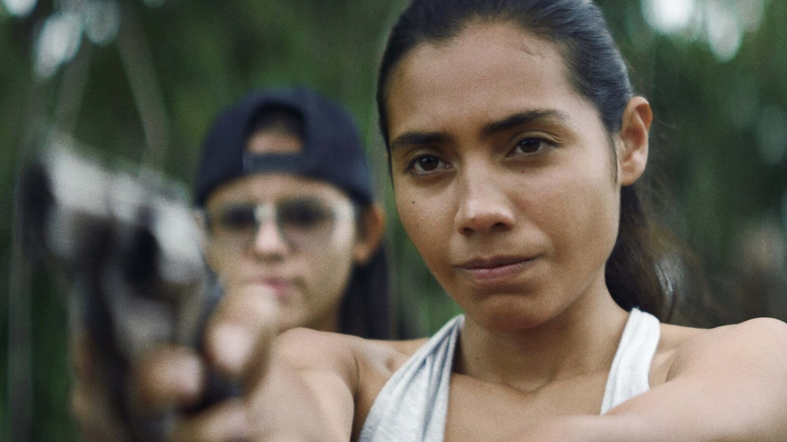 A young woman aims at something with a gun while a man stands behind her