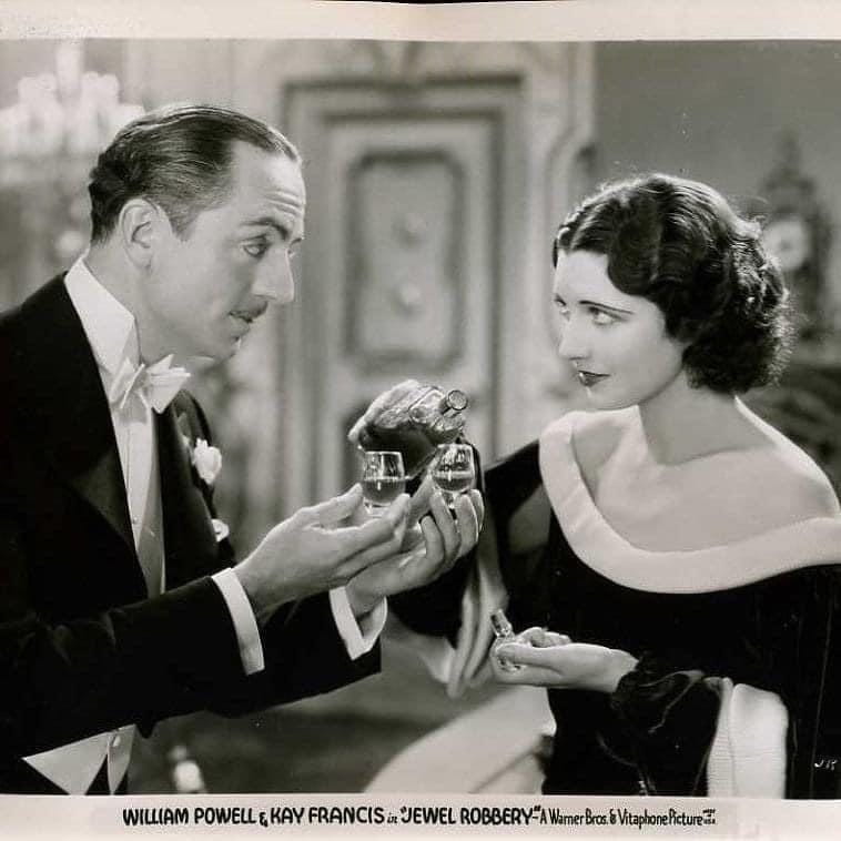 William Powell holds a pair of glasses while Kay Francis pours them drinks