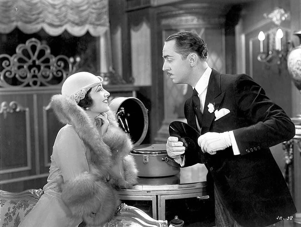 Kay Francis smiles at William Powell as he holds a record