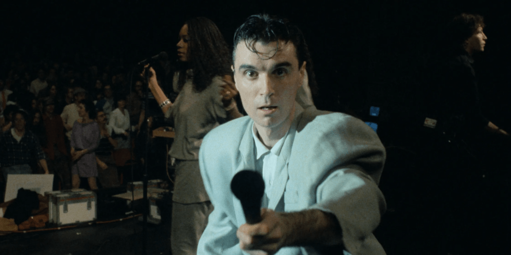 David Byrne offers his microphone to the camera while performing onstage