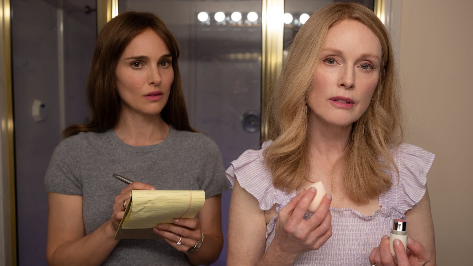 Natalie Portman and Julianne Moore look at each other in a bathroom mirror