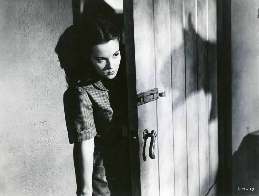 A young woman looks around a door where a leopard's shadow is projected