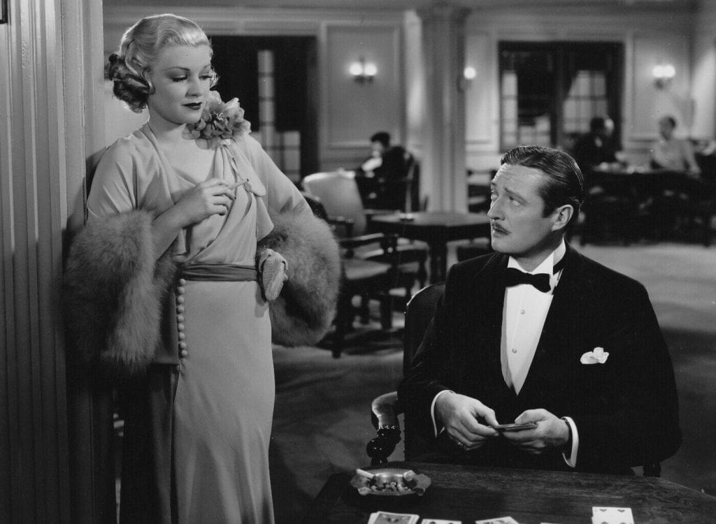 Claire Trevor looks down at Edmund Lowe as he holds a deck of cards
