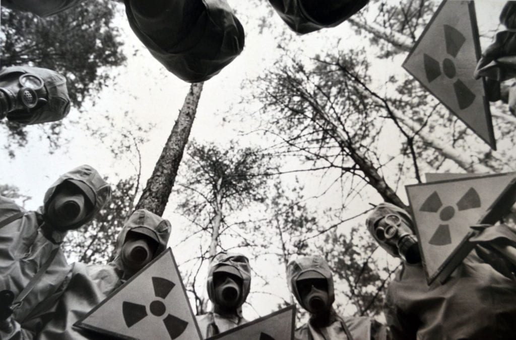 People in gas masks look down at the camera with trees behind them